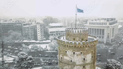 Unique picture of White Tower in Thessaloniki during snowfall and snowstorm with the greek flag waving atop