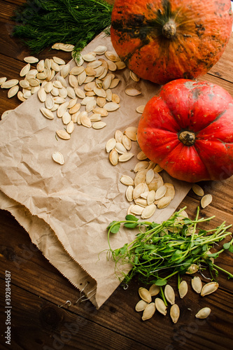 Pumpkin seeds, two pumpkins and micro greens on craft paper and wooden background. Flatley. Top.