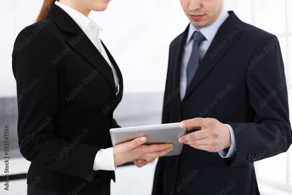 Businessman and woman using tablet computer for discussing questions in office. Partners or colleagues at meeting. Business cooperation concept Businessman and woman using tablet computer for discussing questions in office. Partners or colleagues at meeting. Business cooperation concept