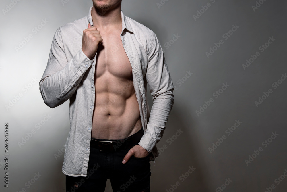 Fit Bodybuilder with defined muscles on grey background wearing dress shirt and jeans Fit Bodybuilder with defined muscles on grey background wearing dress shirt and jeans