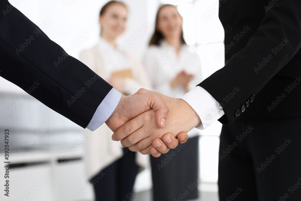 Businessman and woman shaking hands with colleagues at the background. Handshake at meeting in office. Concept of success in business