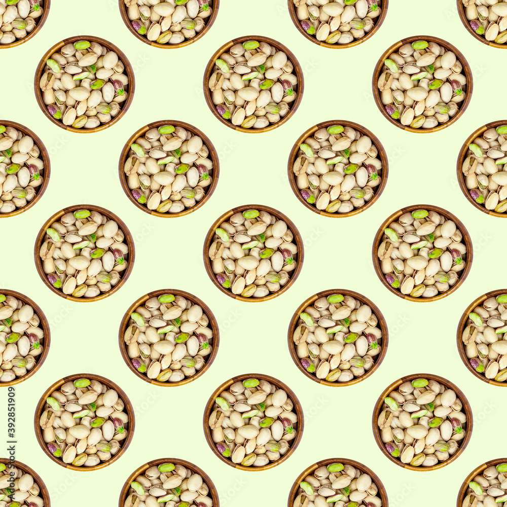 Top view flat lay pistachio nuts in a round wooden bowl repeat seamless pattern on light green background.