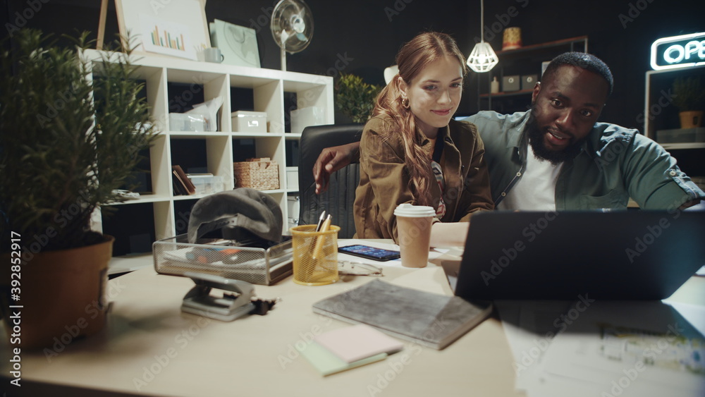 Flirting afro man hugging beautiful lady near laptop in hipster office. Flirting afro man hugging beautiful lady near laptop in hipster office.