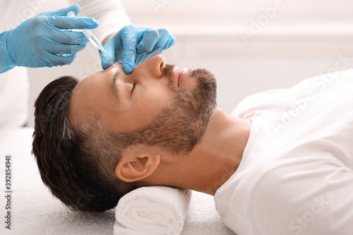 Side view of bearded man getting beauty injection in salon