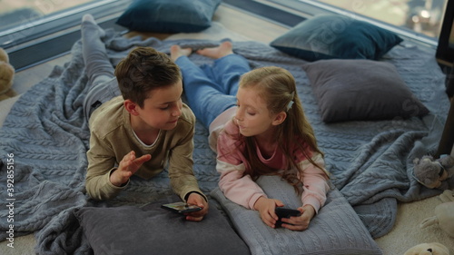 Cute siblings using smartphones indoors. Children giving high five.