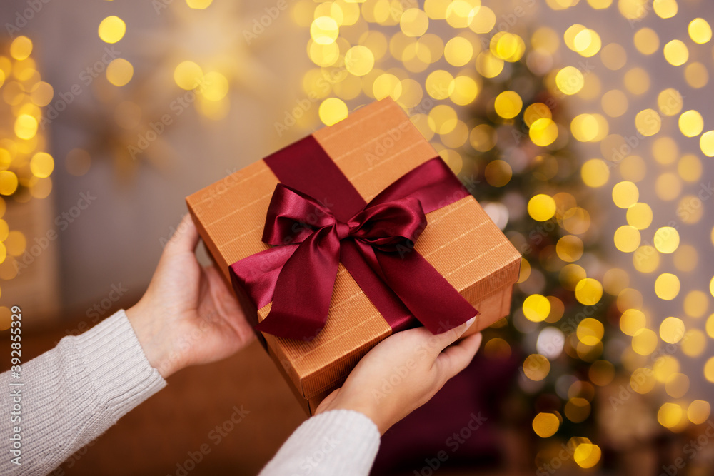 Christmas and new year concept - close up of Christmas present in male hands over festive lights background