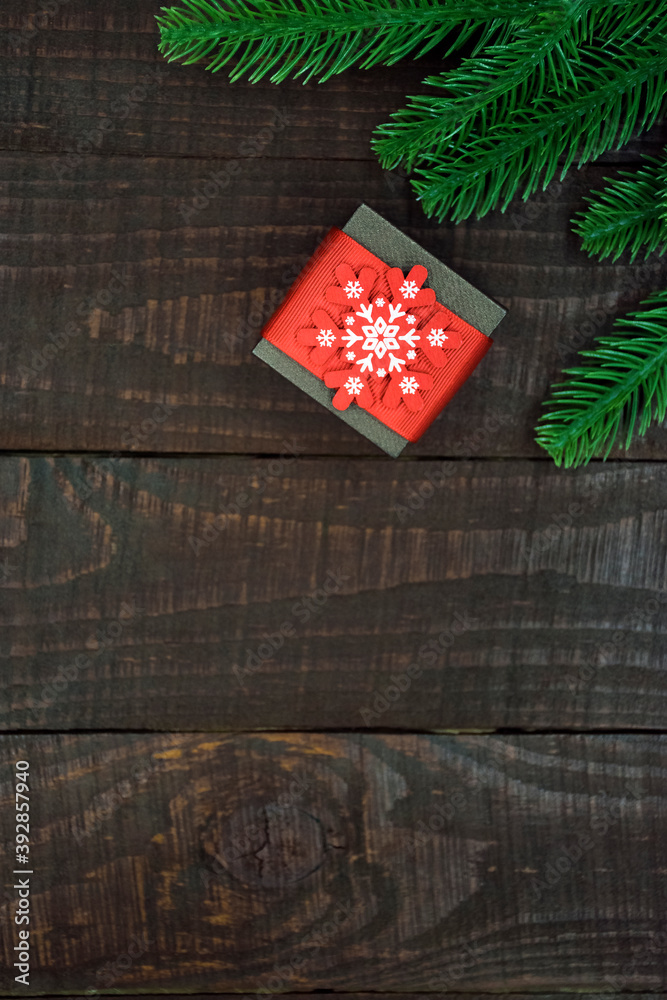Small gift box decorated with white snowflake and red stripe and spruce branches on dark brown wooden background in rustic style. Christmas or New Year gift shopping ideas flat lay with copy space. Small gift box decorated with white snowflake and red stripe and spruce branches on dark brown wooden background in rustic style. Christmas or New Year gift shopping ideas flat lay with copy space.