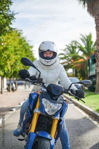 Woman happy with her motorcycle  equipped with helmet and white jacket