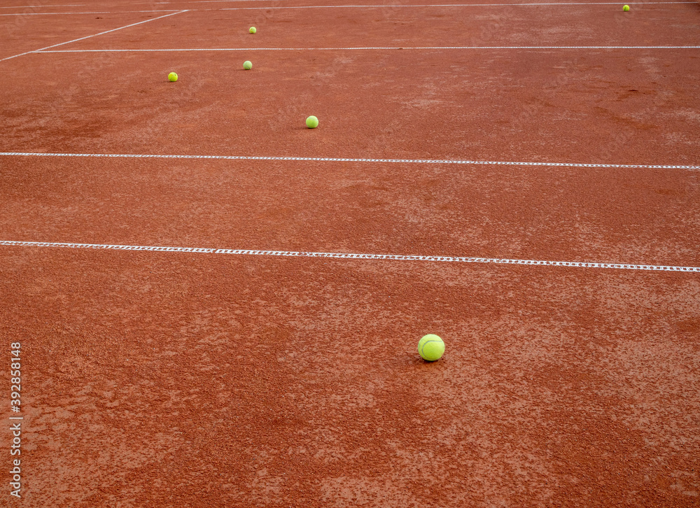 Many balls for tennis laying on a red tennis clay court