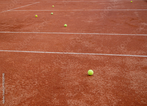 Many balls for tennis laying on a red tennis clay court