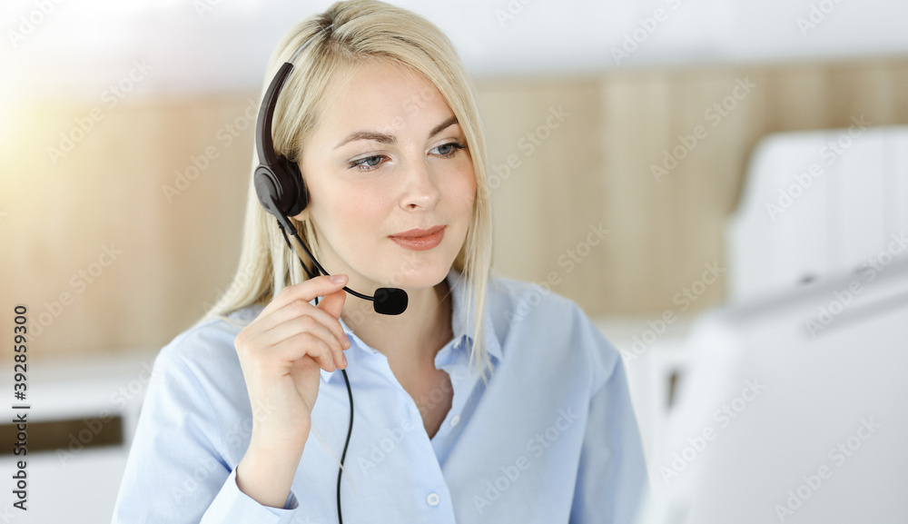Blonde business woman sitting and communicated by headset in call center in sunny office. Concept of telesales business Blonde business woman sitting and communicated by headset in call center in sunny office. Concept of telesales business