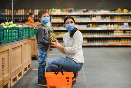 Mother and her son wearing protective face mask shop at a supermarket during the coronavirus epidemic