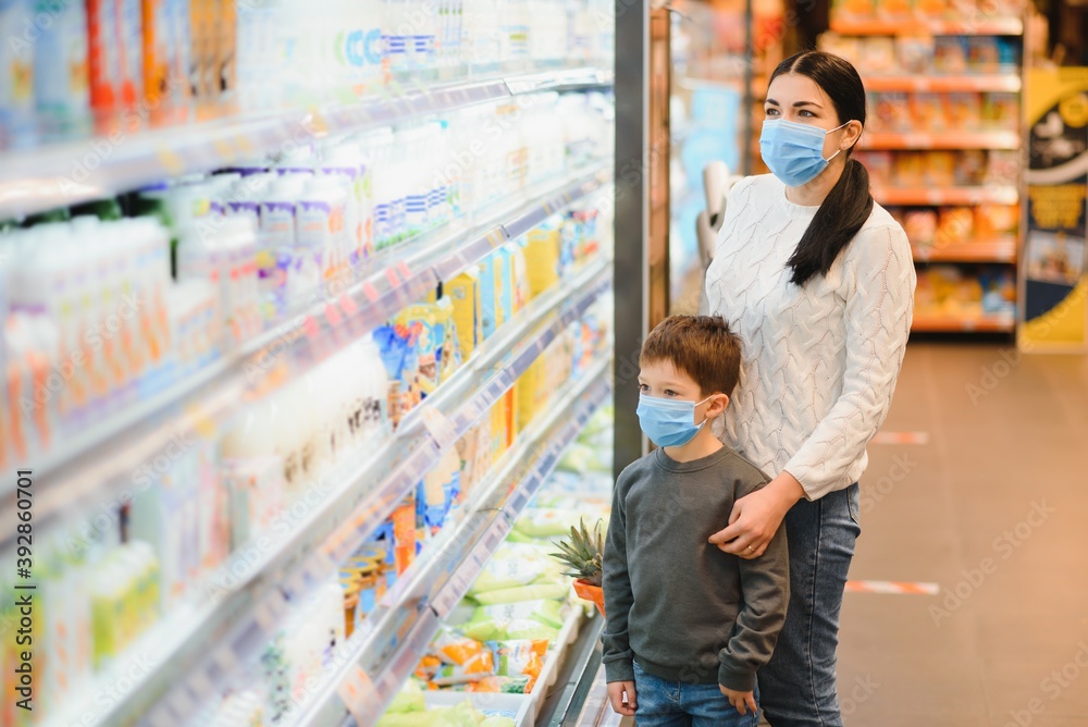 Shopping with kids during virus outbreak. Mother and child wearing surgical face mask buying fruit in supermarket. Mom and little boy buy fresh vegetable in grocery store. Family in shop.