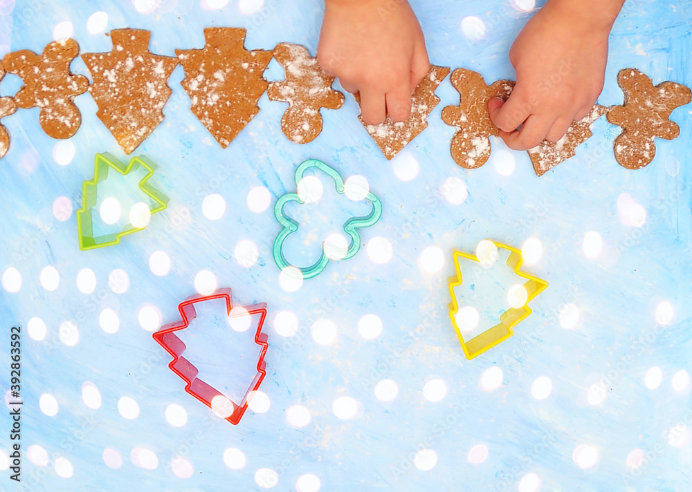 Girl makes christmas cookies, ginger man on blue background with bokeh lights.