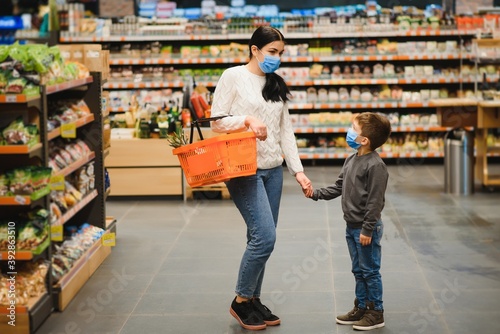Mother and her son wearing protective face mask shop at a supermarket during the coronavirus epidemic