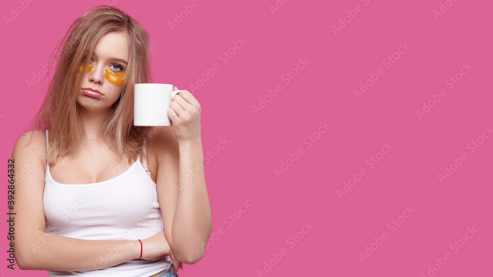 Woman with headache and hangover holding cup with hot drink on pink isolated background Woman with headache and hangover holding cup with hot drink on pink isolated background