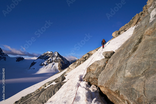 mountaineer thethered to a rope climbing up a snowy mounatin side in summer with Petit Mont Colon in the background
