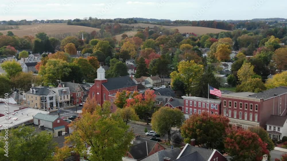 Small Town America. Aerial establishing shot of homes and church with American flag flying in breeze. Drone orbit.