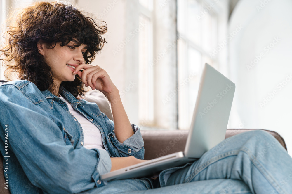Joyful curly girl using laptop and smiling while sitting on sofa Joyful curly girl using laptop and smiling while sitting on sofa