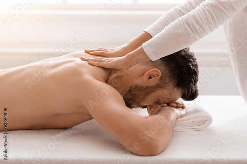 Side view of relaxed man having body massage at spa