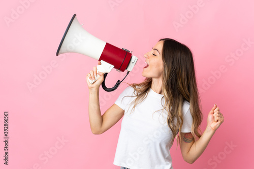 Young Romanian woman isolated on pink background shouting through a megaphone to announce something in lateral position photo