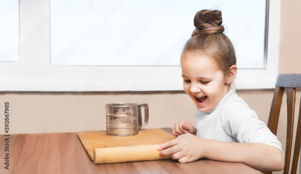 cute preschoolgirl girl is sitting at the table and is going to prepare the dough for modeling. cooking concept. on the kitchen cute preschoolgirl girl is sitting at the table and is going to prepare the dough for modeling. cooking concept. on the kitchen