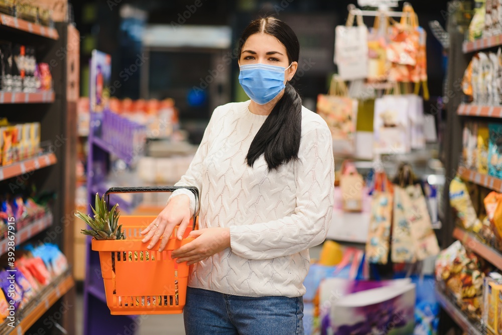 Young woman with face mask walking through grocery store during COVID-19 pandemic.