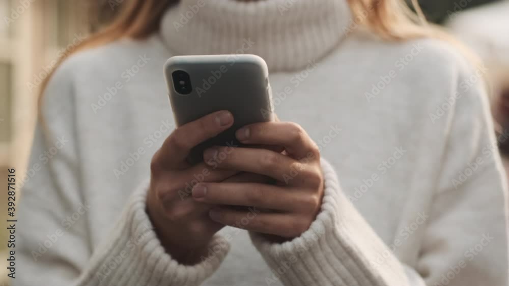 Close up woman in white cozy sweater texting with friends in online chat on smartphone outdoor Close up woman in white cozy sweater texting with friends in online chat on smartphone outdoor