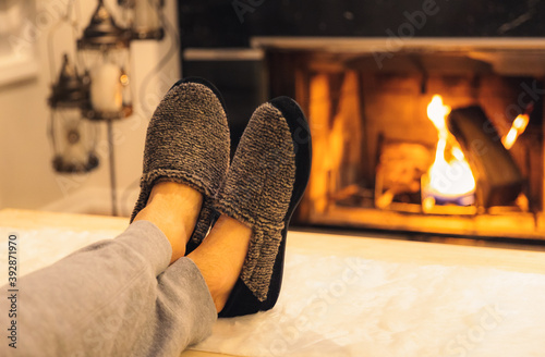 Man in slippers relaxing with his feet up - warm cozy cabin scene with a fireplace in the background. 