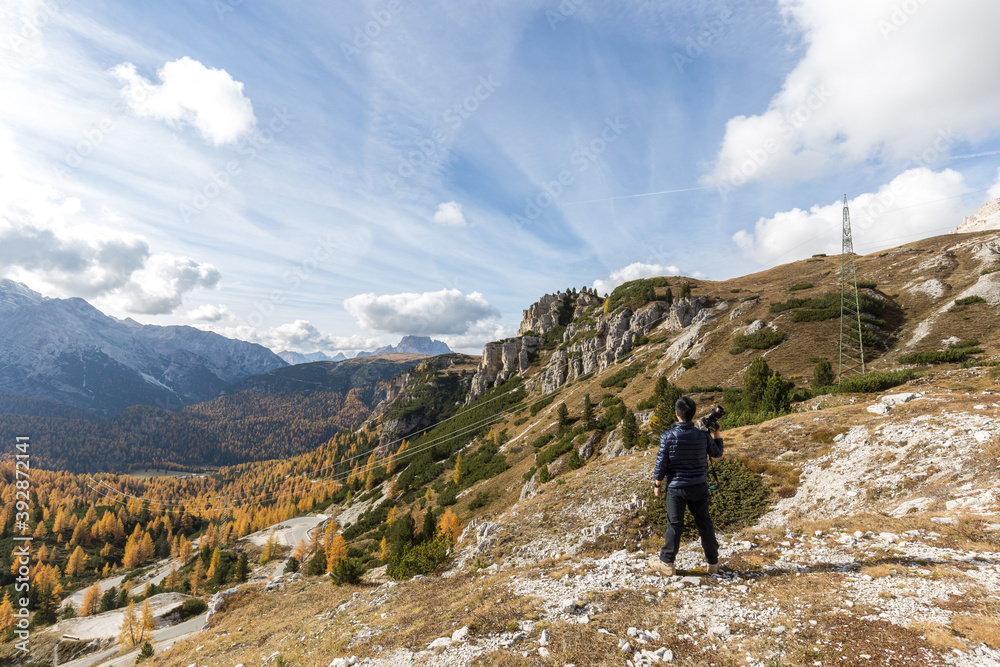 A man holding a camera at mountain edge in Dolomites in autumn