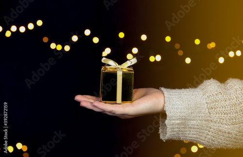 hand holding a gold gift box with gold ribbon,bokeh sparkle background, Christmas or Birthday present concept with space for text