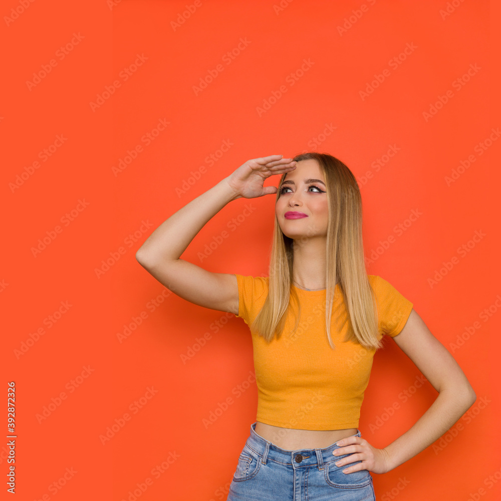 Young Woman In Orange Shirt Holding Hand On Forehead And Looking Away