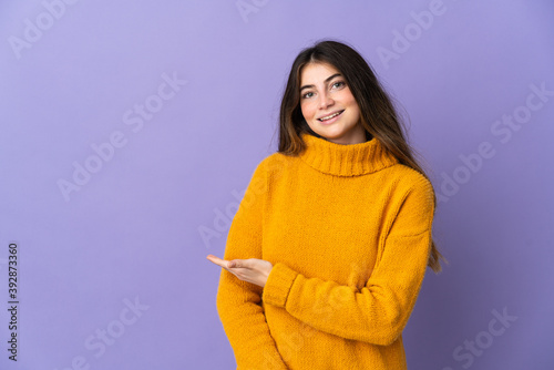 Young caucasian woman isolated on purple background presenting an idea while looking smiling towards