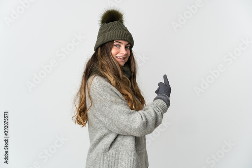 Young caucasian woman with winter hat isolated on white background pointing back