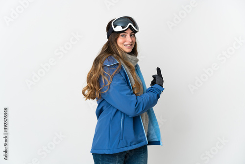 Skier girl with snowboarding glasses isolated on white background pointing back