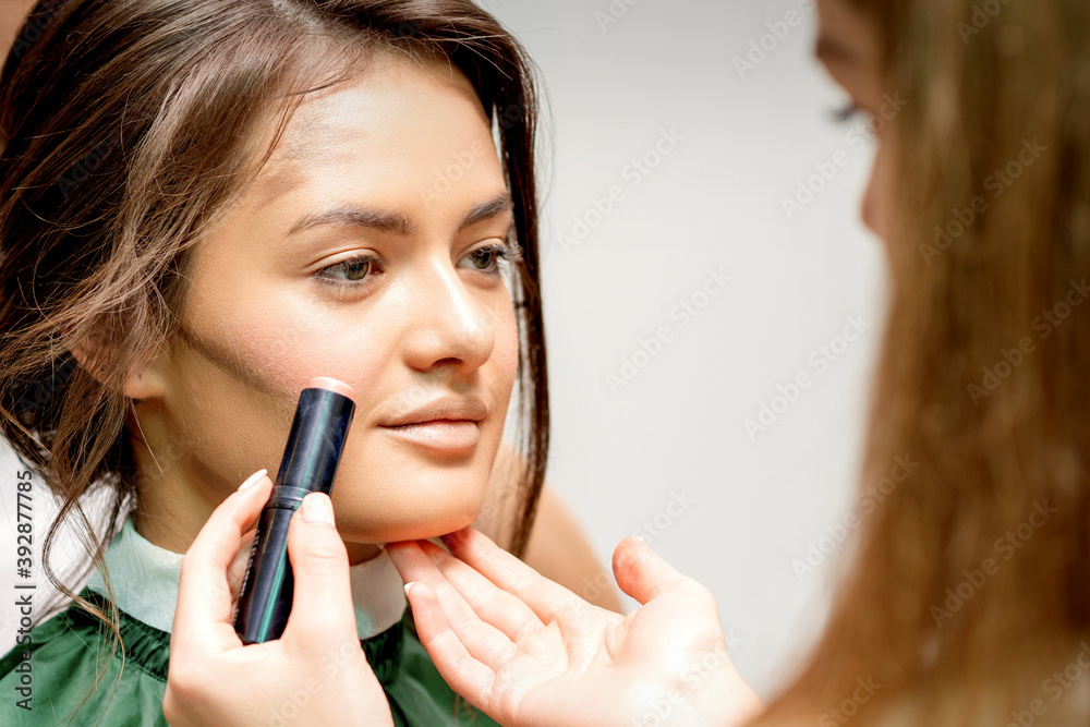 Makeup artist applying cream blush stick foundation on cheek of young caucasian woman Makeup artist applying cream blush stick foundation on cheek of young caucasian woman