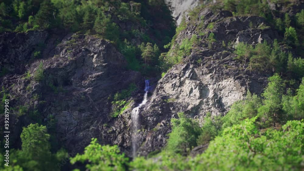 One of the waterfalls on the shores of the Naeroy fjord, Norway. A narrow stream of water cascading from the jagged cliff. Lush vegetation covering the steep mountainsides. One of the waterfalls on the shores of the Naeroy fjord, Norway. A narrow stream of water cascading from the jagged cliff. Lush vegetation covering the steep mountainsides.