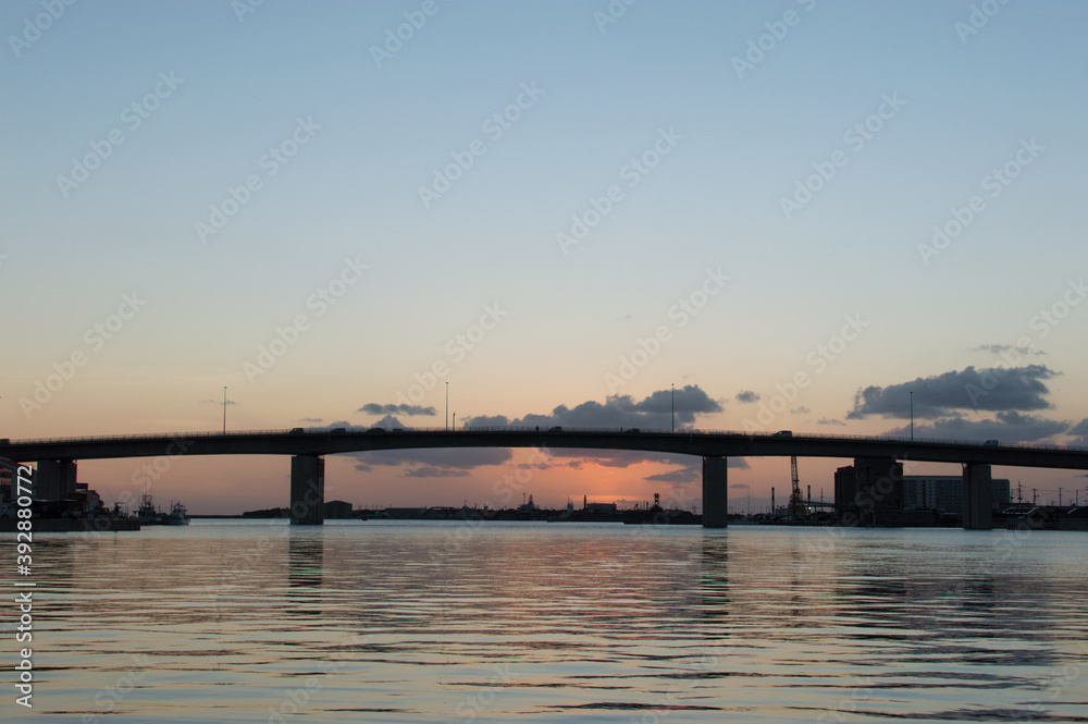 オレンジ色の夕焼けとシルエットの高架橋のある凪の港