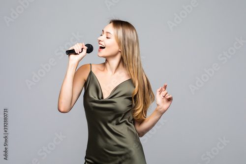 Beautiful young woman singing to microphone isolated on grey background