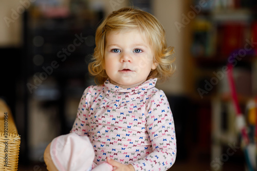 Adorable cute little toddler girl playing with doll. Happy healthy baby child having fun with role game, playing mother at home or nursery. Active daughter with toy.