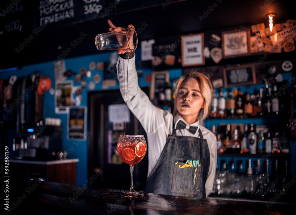 Confident girl barman intensely finishes his creation at bar