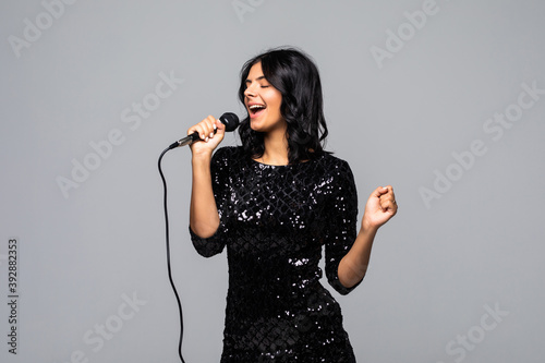 Beautiful brunette woman singing to microphone isolated on gray background
