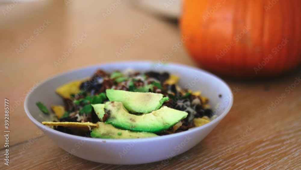 Female hand picking nachos covered with cheese and beans from a bowl