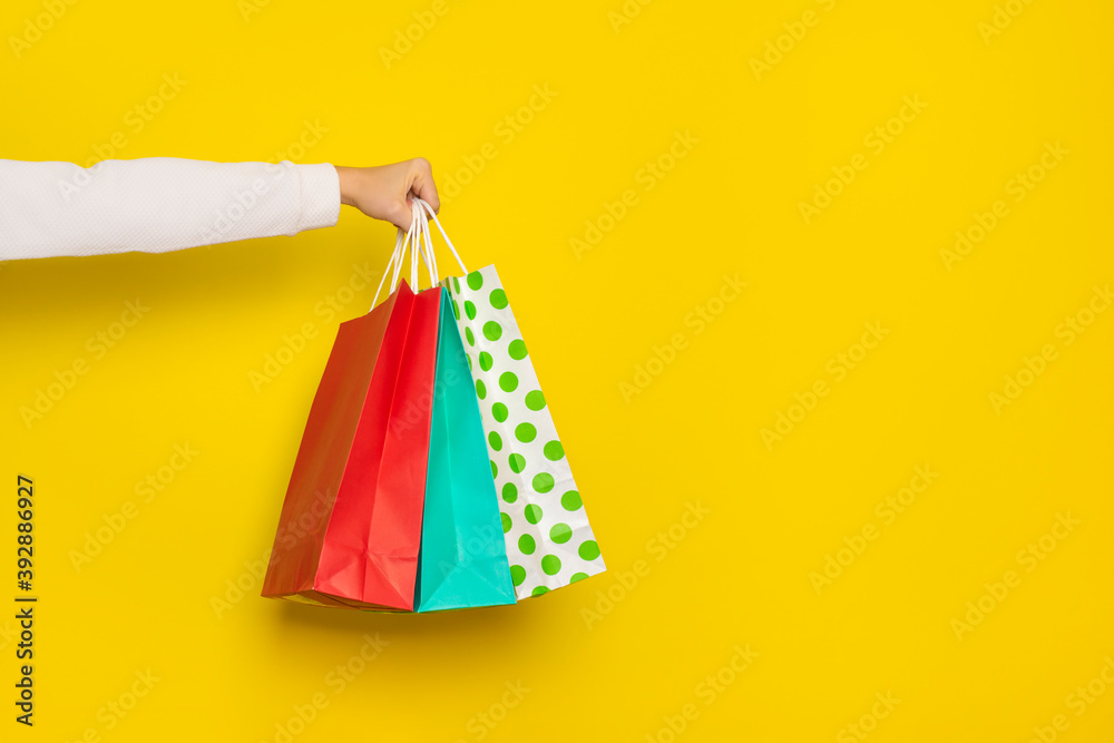 Female hand holds shopping paper bags isolated on yellow background.