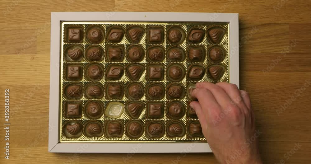 Box of chocolate bonbon candies put on a table and hands taking pieces