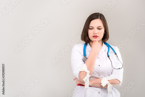 Portrait of beautiful young doctor with pensive face on light background