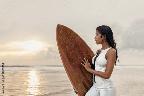 A girl of oriental appearance is resting on the sea and posing for the camera with a surf on a background of sunset and cloudy sky