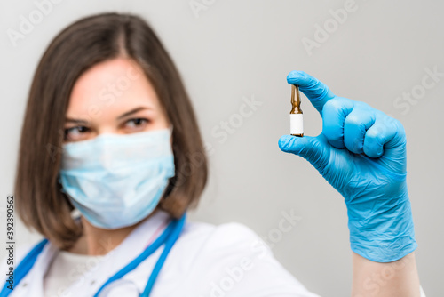 Portrait of young beautiful doctor shows ampoule in hands on light background