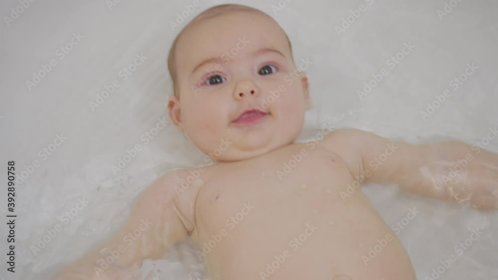 A nice little caucasian newborn baby is funny smiling, lying at the back in the bath. Portrait of a playful and energetic child close-up. A nice little caucasian newborn baby is funny smiling, lying at the back in the bath. Portrait of a playful and energetic child close-up.
