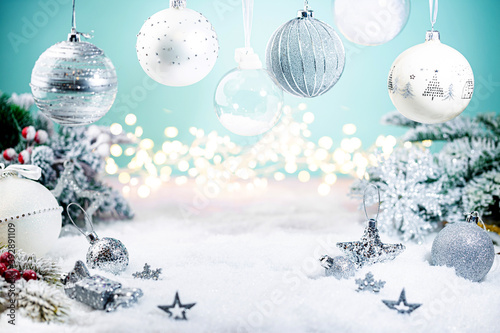 Christmas silver and white decorations on snow with fir tree branches and christmas lights on blue background